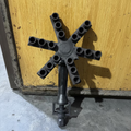 A dark cast iron six-arm candle holder or multi-light fixture with a central hub and six cylindrical sockets, shown against a yellow wooden door background.