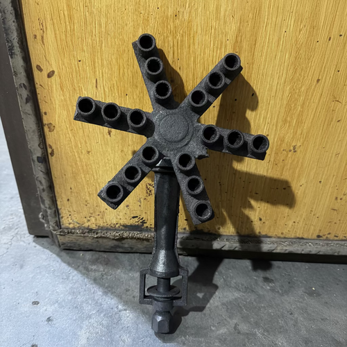 A dark cast iron six-arm candle holder or multi-light fixture with a central hub and six cylindrical sockets, shown against a yellow wooden door background.