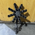 A dark cast iron star-shaped tool with multiple cylindrical sockets on each of its eight spokes, mounted on a central post with a bracket at the bottom, photographed against a yellow wooden surface.