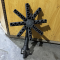 A vintage cast iron multi-arm sprinkler head or decorative metal fixture, photographed against a yellow wooden door and concrete floor.