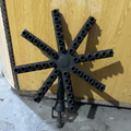 A vintage rusted metal sprinkler head with multiple nozzles, photographed leaning against a wooden wall on a concrete floor.