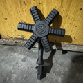 A dark gray cast iron six-spoke wheel handle with a textured grip pattern on each arm and a central circular emblem, resting on a concrete floor against a wooden wall.