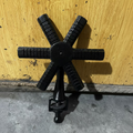 A vintage cast iron six-spoke wheel valve stem cap with ribbed spokes and a threaded stem, shown against a yellow wooden background.