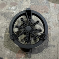 A circular cast iron burner grate or stove component with multiple circular openings and curved metal support arms, photographed from above on a rough stone floor.